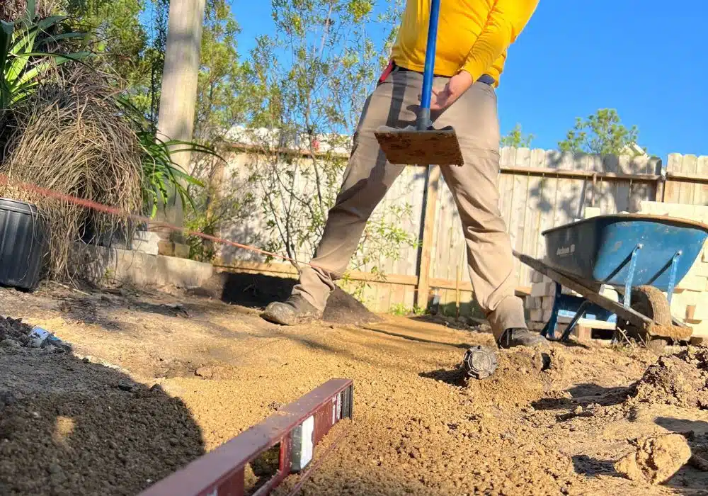 man tamping down base with a level and string line preparing for a garden