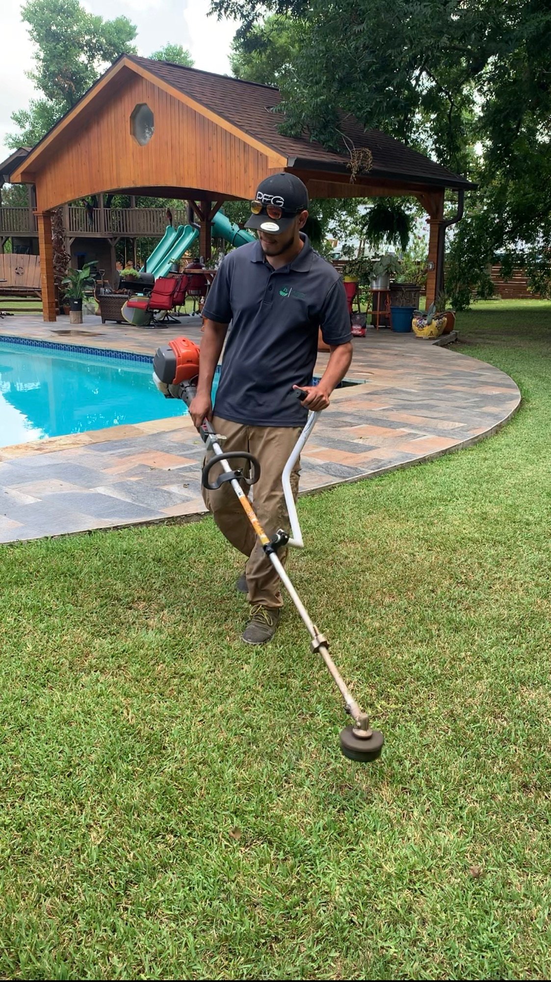 Jorge, one of the onwers holding a professional lawn trimmer with freshly trimmed grass in the background