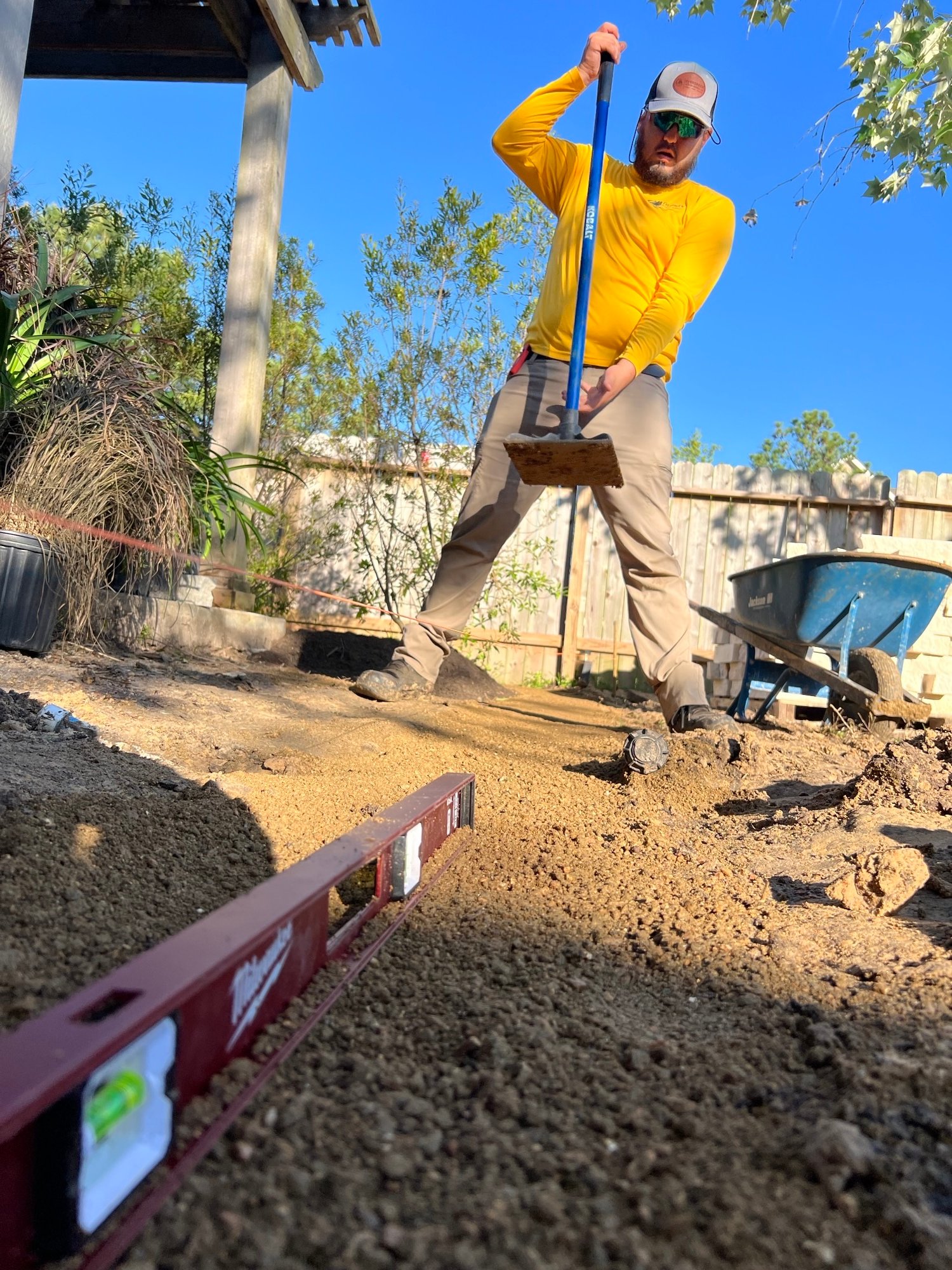 Gardener performing landscape construction by tamping down and preparing the base for garden edging – Evergreen Outdoor Services SATISFACTION GUARANTEED
