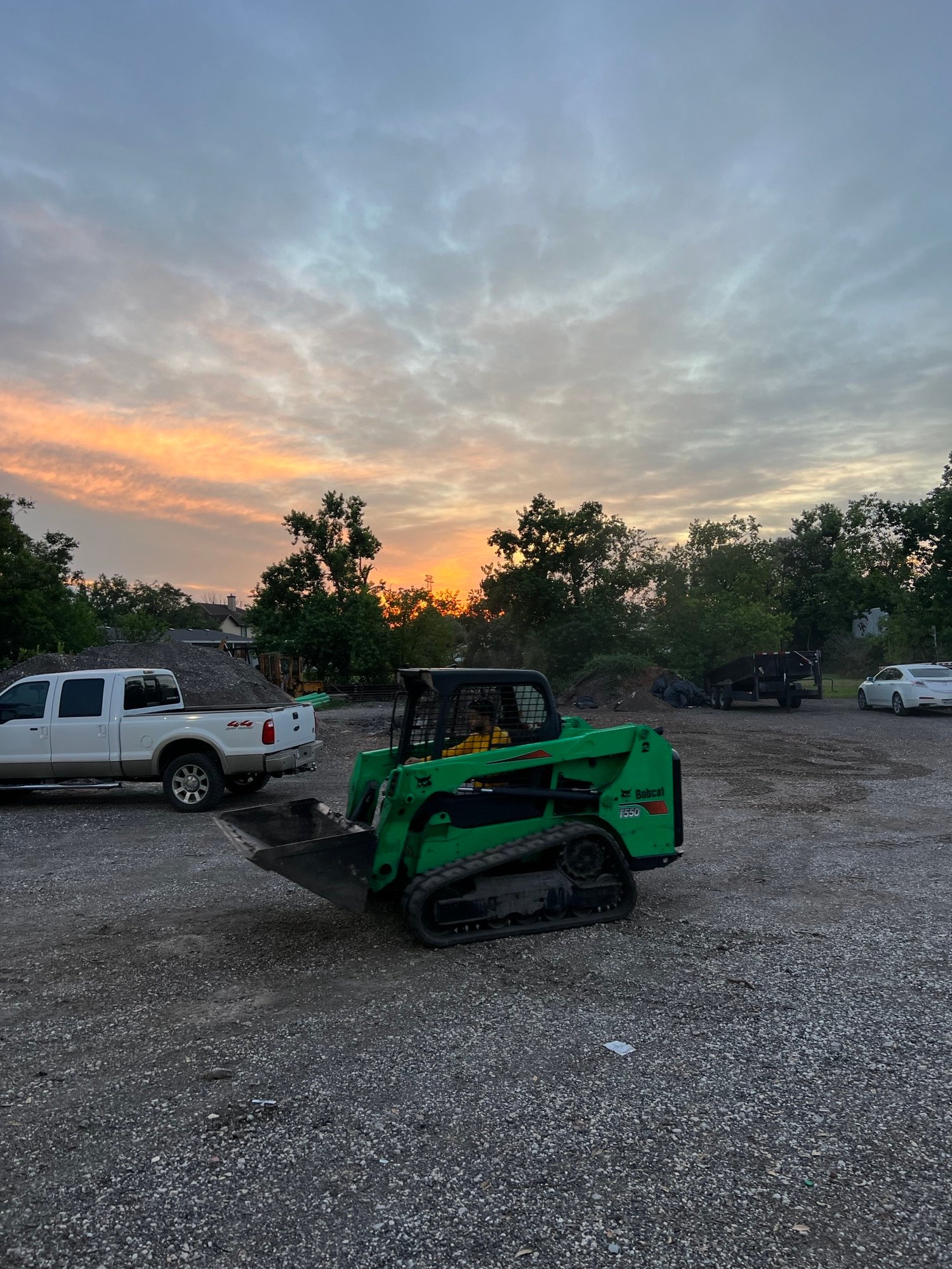 Skid steer in operation at our shop yard during sunset, with Jeffrey, one of the owners, at the controls.