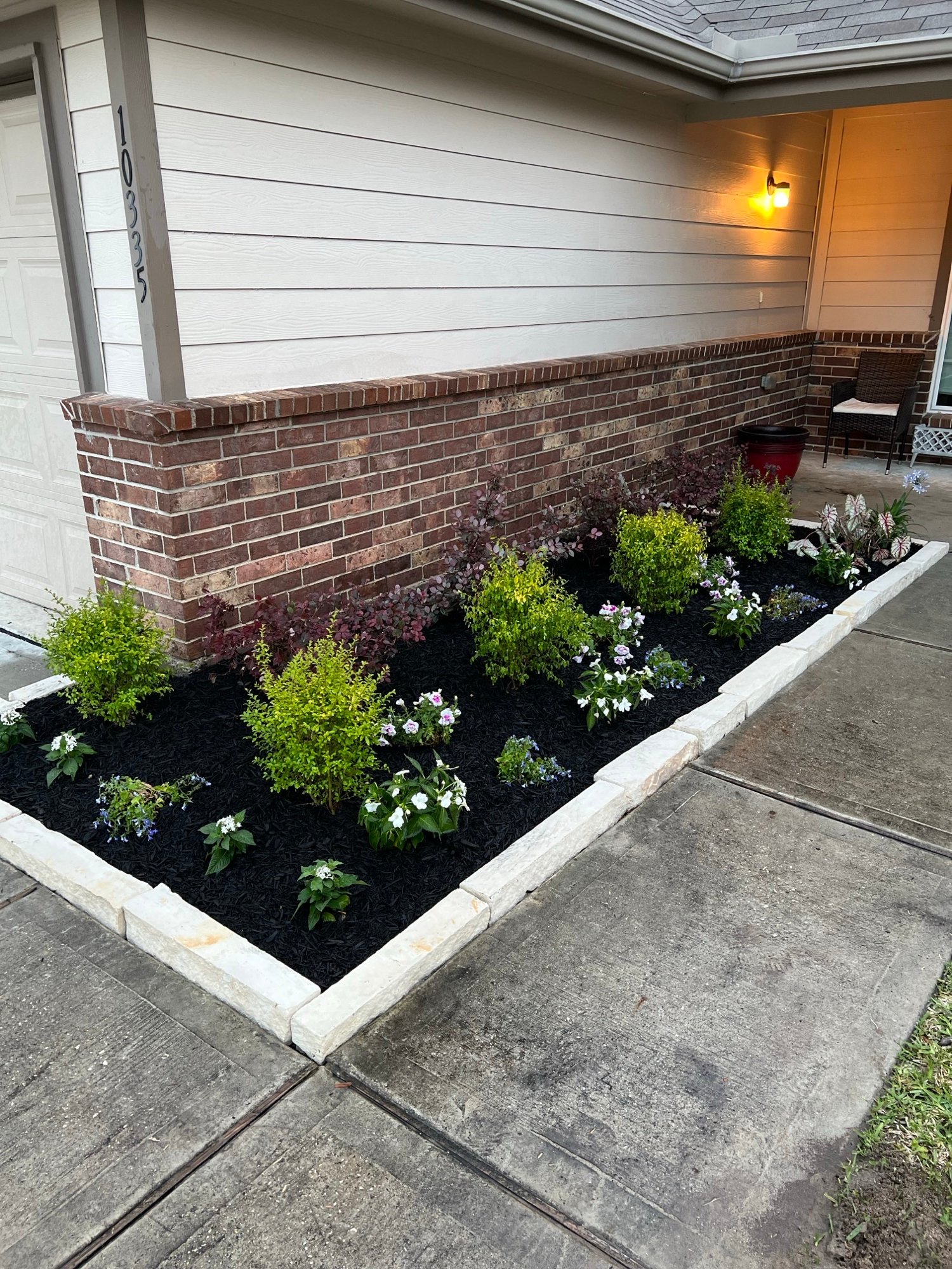 Complete stone border garden installation featuring evergreen shrubs like Sunshine Ligustrum and Loropetalum, accented with seasonal blooms for a modern, year-round landscape design in Hidden Meadows neighborhood