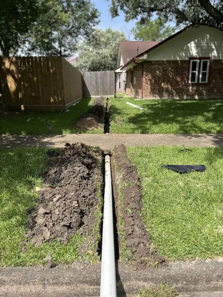 Drainage installation in progress showing a buried PVC pipe system extending from the backyard to the curb, designed to redirect stormwater and prevent lawn flooding in a Houston residential yard.