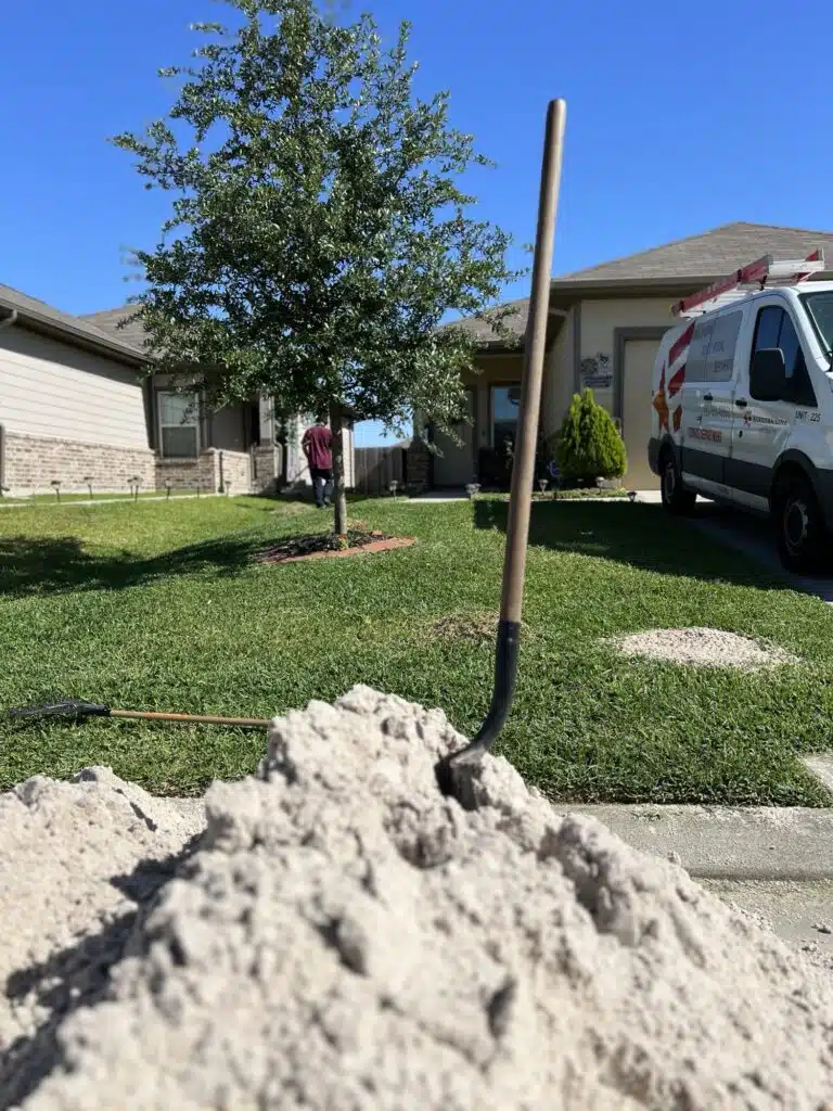 Close-up of sand pile with shovel during a residential lawn leveling project in Houston, with visible patch leveling areas and landscaping tools on a sunny day.