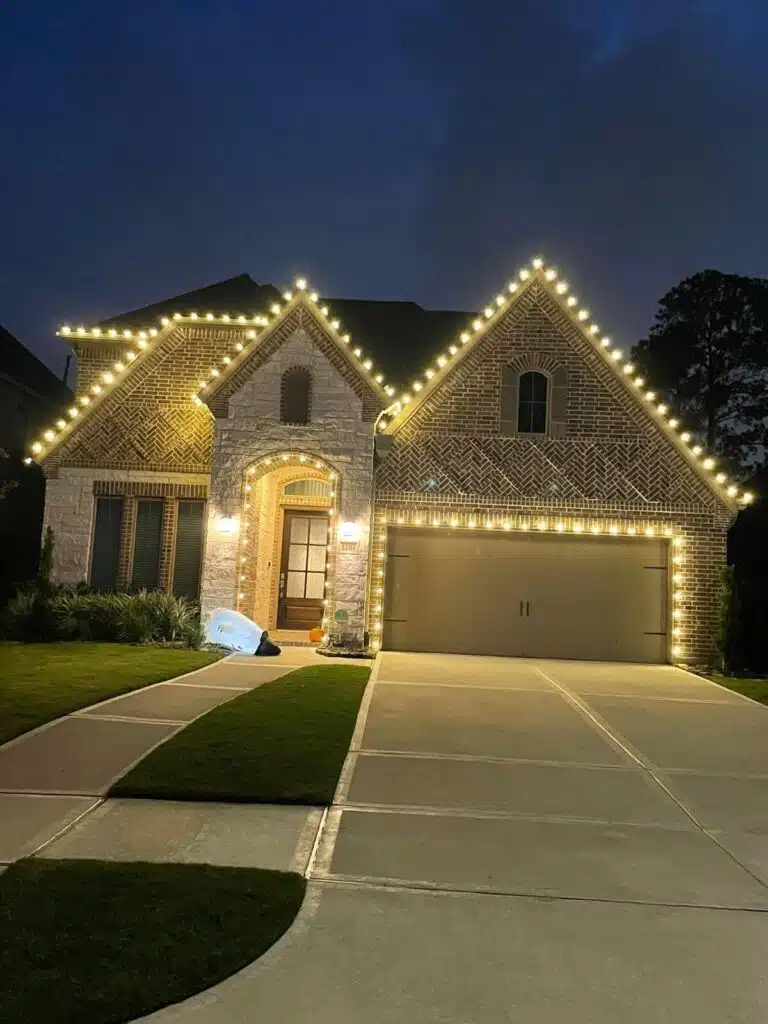 Warm white holiday lights outlining the roof and garage of a brick home in the Summerwood and Atascocita area of Houston, showing holiday lighting tips for Houston homeowners in action